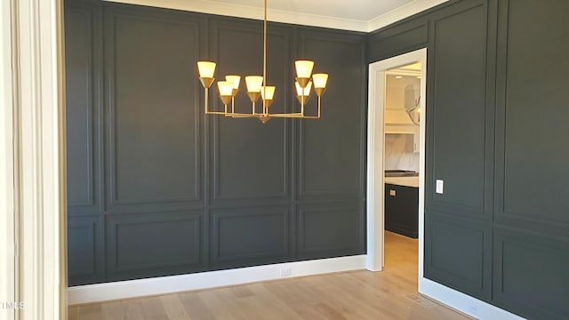 unfurnished dining area with a notable chandelier, light wood-type flooring, and a decorative wall