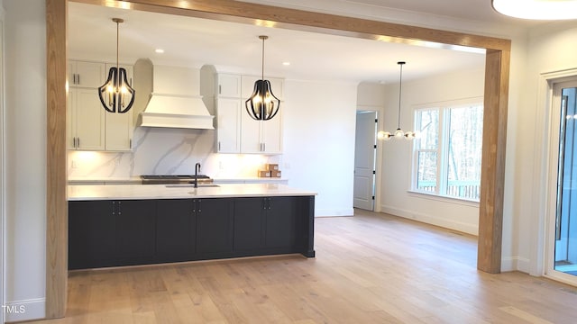 kitchen featuring light countertops, backsplash, light wood-style floors, white cabinetry, and premium range hood