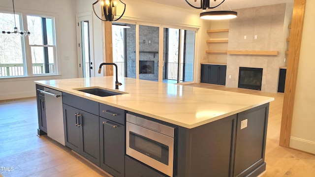 kitchen with stainless steel appliances, a tiled fireplace, light wood-style floors, open floor plan, and a sink