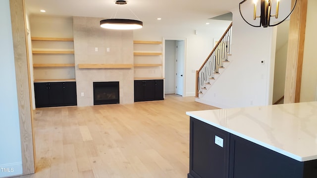 unfurnished living room featuring light wood finished floors, built in features, stairs, a fireplace, and recessed lighting