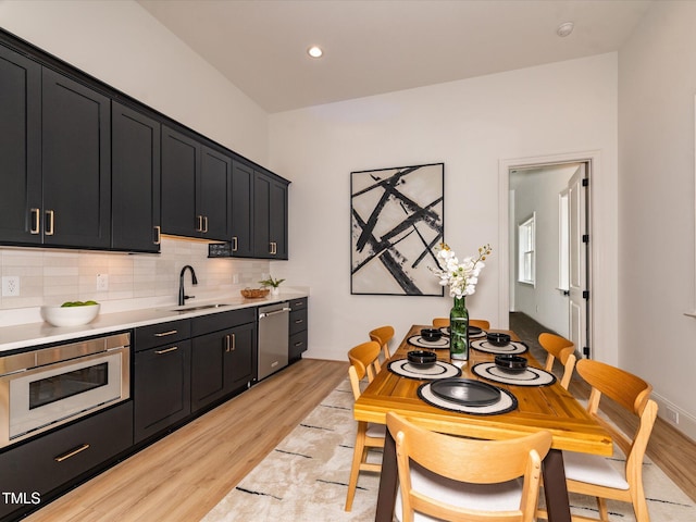 122 W Beech Slope Ct, Chapel Hill, NC 27517 - kitchen with appliances with stainless steel finishes, a sink, light wood finished floors, dark cabinets, and backsplash