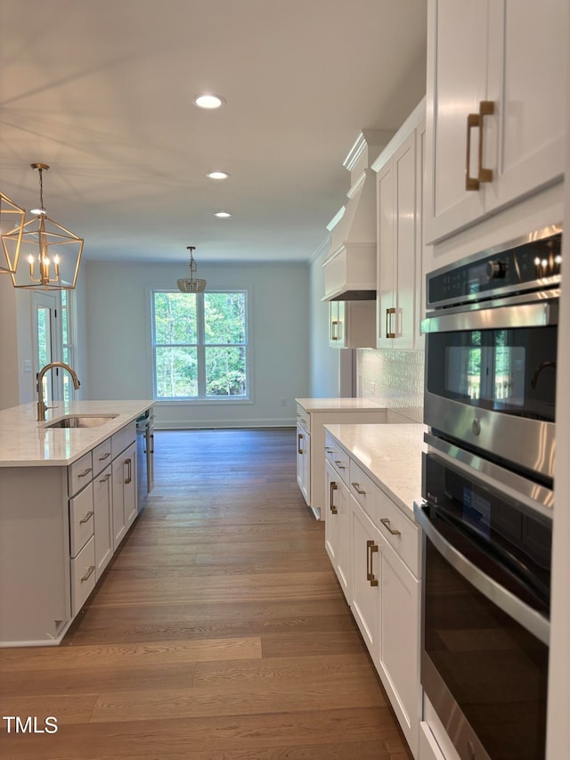 kitchen with appliances with stainless steel finishes, white cabinets, hardwood / wood-style flooring, a kitchen island with sink, and sink