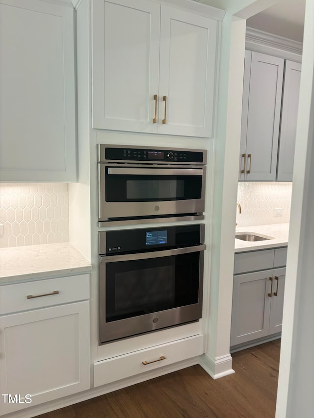 kitchen with tasteful backsplash, white cabinets, dark hardwood / wood-style flooring, light stone countertops, and double oven