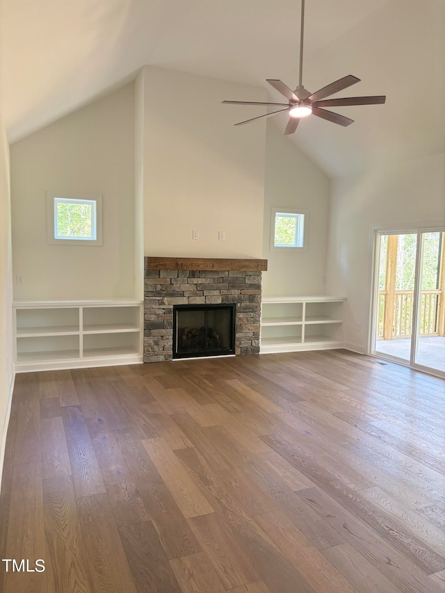 unfurnished living room featuring a wealth of natural light, ceiling fan, hardwood / wood-style flooring, and a stone fireplace