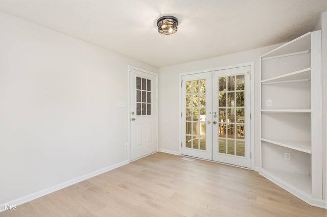 empty room featuring light hardwood / wood-style floors, french doors, and a textured ceiling