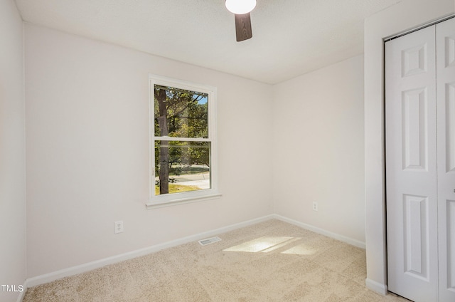 empty room with a textured ceiling, light colored carpet, and ceiling fan