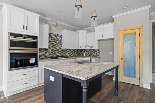 kitchen featuring appliances with stainless steel finishes, a center island with sink, backsplash, and white cabinets