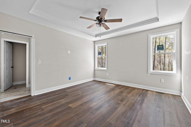 empty room with dark hardwood / wood-style flooring, ceiling fan, and a raised ceiling