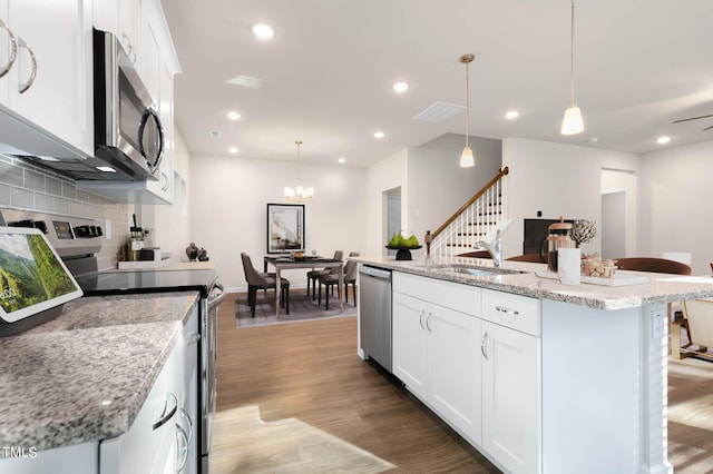 kitchen with appliances with stainless steel finishes, an island with sink, hanging light fixtures, and white cabinets