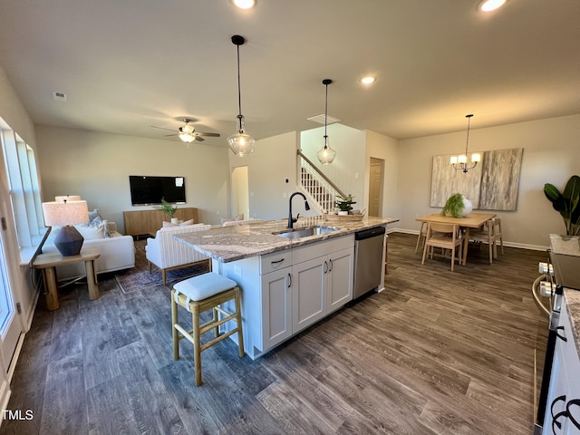 kitchen with appliances with stainless steel finishes, white cabinetry, hanging light fixtures, light stone counters, and a center island with sink