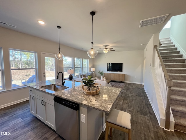 kitchen featuring sink, dishwasher, light stone counters, white cabinets, and a center island with sink