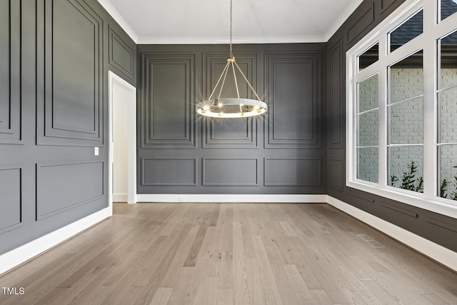 unfurnished dining area with a chandelier, light wood-type flooring, and ornamental molding