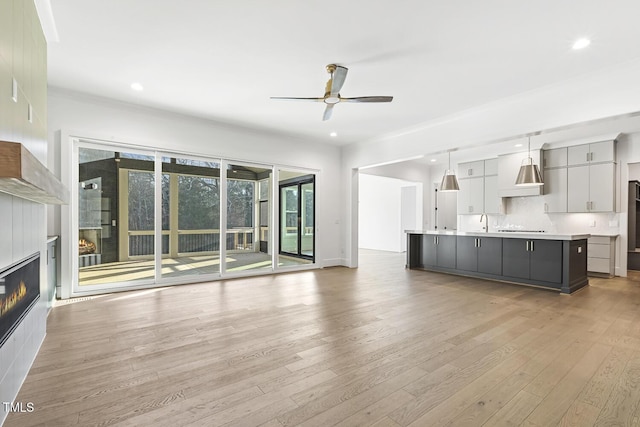 unfurnished living room with ceiling fan, crown molding, light wood-type flooring, and sink