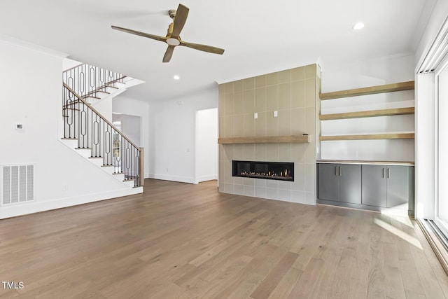 unfurnished living room with a tile fireplace, wood-type flooring, and ceiling fan