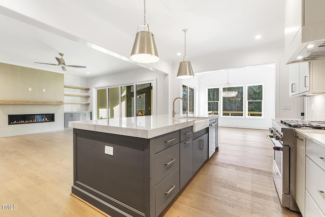 kitchen featuring a large fireplace, stainless steel appliances, pendant lighting, a kitchen island with sink, and white cabinets