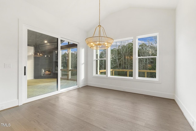 unfurnished dining area with a large fireplace, hardwood / wood-style floors, lofted ceiling, and a notable chandelier