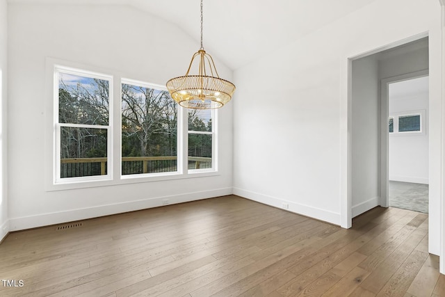 unfurnished dining area with hardwood / wood-style flooring, lofted ceiling, and a notable chandelier