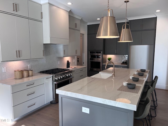 kitchen featuring sink, stainless steel appliances, gray cabinetry, and an island with sink