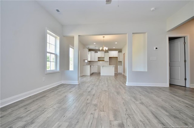 unfurnished living room featuring an inviting chandelier and light hardwood / wood-style floors