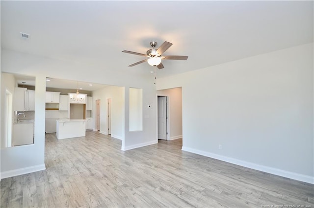 unfurnished living room featuring sink, ceiling fan with notable chandelier, and light hardwood / wood-style flooring