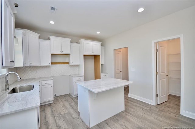 kitchen with sink, light stone counters, light wood-type flooring, a kitchen island, and white cabinets