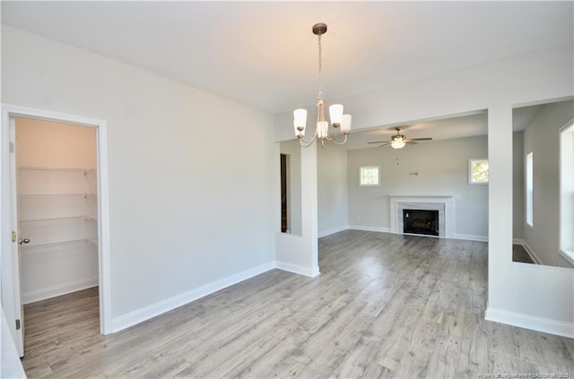 unfurnished living room with ceiling fan with notable chandelier and light hardwood / wood-style floors