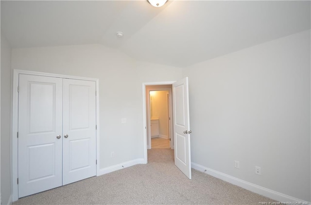 unfurnished bedroom with light colored carpet, lofted ceiling, and a closet