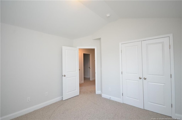 unfurnished bedroom featuring vaulted ceiling, light colored carpet, and a closet