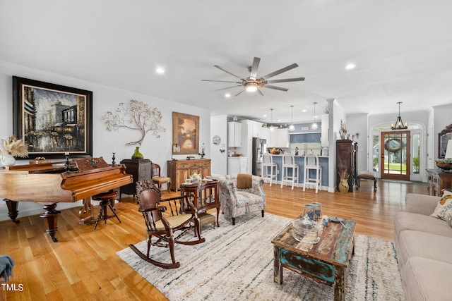 living room with crown molding, ceiling fan with notable chandelier, and light hardwood / wood-style floors