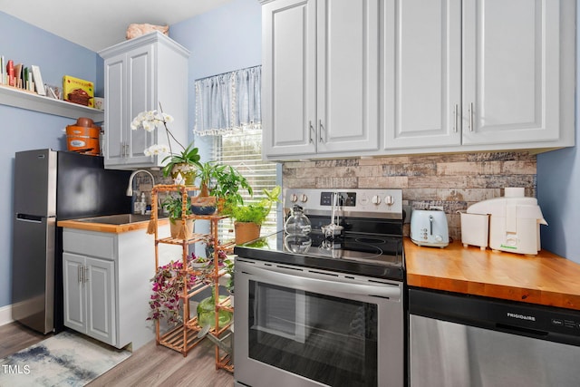 kitchen with backsplash, white cabinetry, light hardwood / wood-style floors, and stainless steel appliances