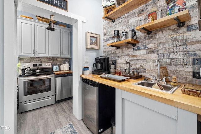 kitchen featuring appliances with stainless steel finishes, light hardwood / wood-style floors, white cabinetry, butcher block counters, and sink