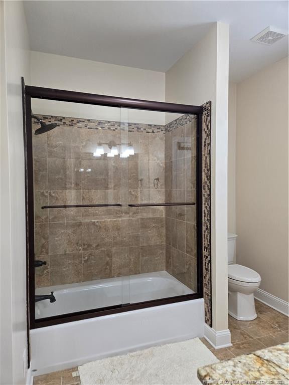 bathroom featuring combined bath / shower with glass door, tile floors, and toilet