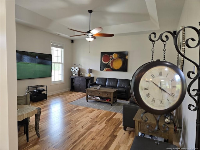 living room with a raised ceiling, ceiling fan, and light wood-type flooring