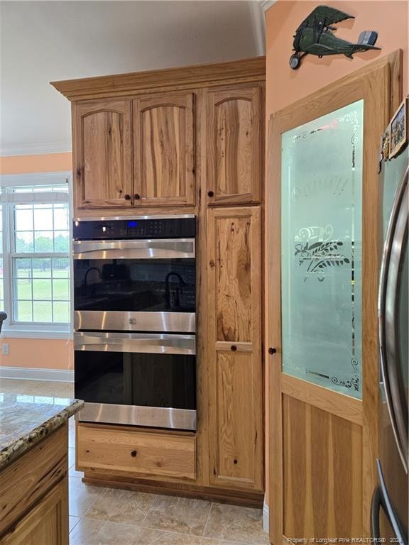 kitchen featuring light stone countertops, double oven, light tile flooring, fridge, and crown molding