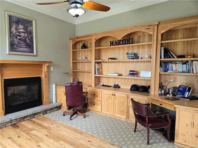 office with ceiling fan, crown molding, light hardwood / wood-style flooring, and a stone fireplace