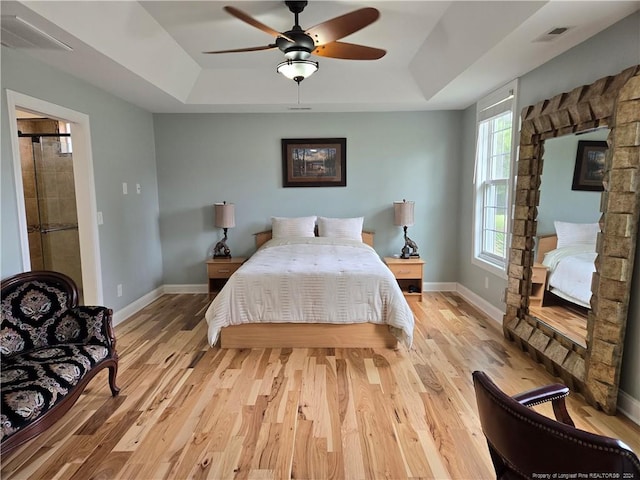 bedroom featuring ceiling fan, a tray ceiling, and light wood-type flooring