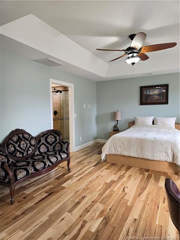 bedroom with ceiling fan, a tray ceiling, and light hardwood / wood-style floors