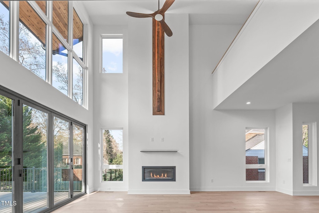 unfurnished living room with ceiling fan, light hardwood / wood-style floors, and a towering ceiling