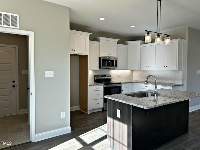 kitchen featuring white cabinetry, light stone counters, stainless steel appliances, and an island with sink