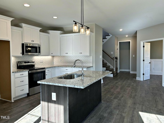 kitchen with sink, a center island with sink, appliances with stainless steel finishes, pendant lighting, and white cabinets