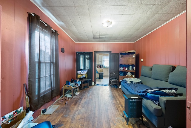 living room with ornamental molding, wooden walls, and wood-type flooring