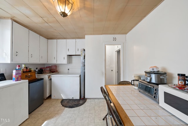 kitchen with washer / dryer, refrigerator, light tile floors, and white cabinets