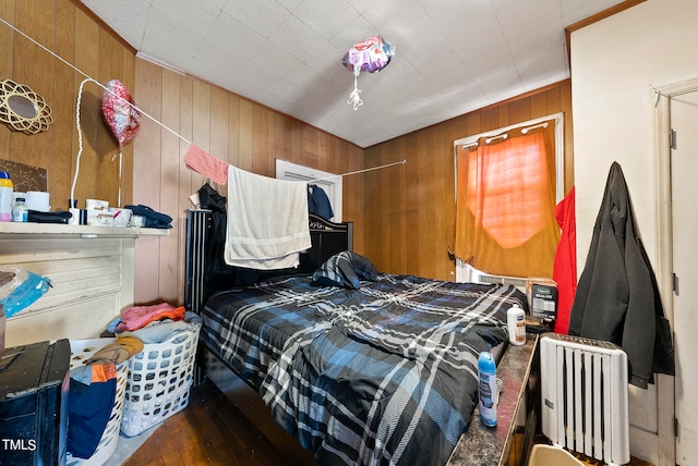 bedroom with radiator heating unit, dark hardwood / wood-style flooring, and wood walls