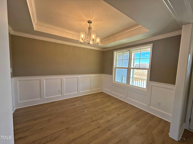 spare room with a notable chandelier, ornamental molding, dark wood-type flooring, and a raised ceiling