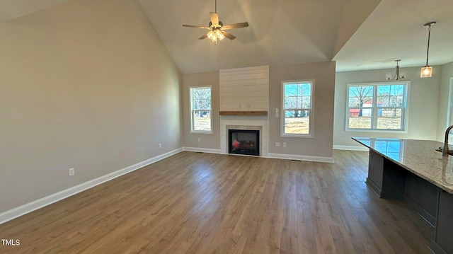 unfurnished living room featuring hardwood / wood-style flooring, a tile fireplace, high vaulted ceiling, and ceiling fan