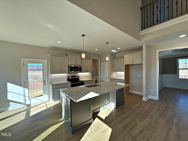 kitchen featuring sink, stainless steel appliances, light stone counters, a center island with sink, and decorative light fixtures