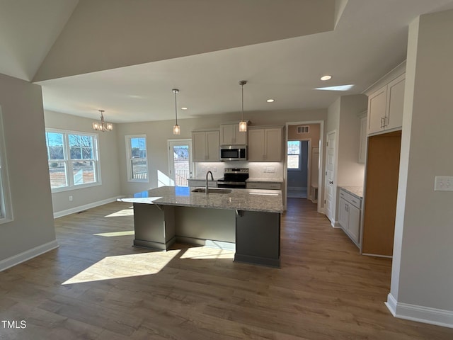 kitchen featuring sink, appliances with stainless steel finishes, a kitchen island with sink, hanging light fixtures, and light stone counters