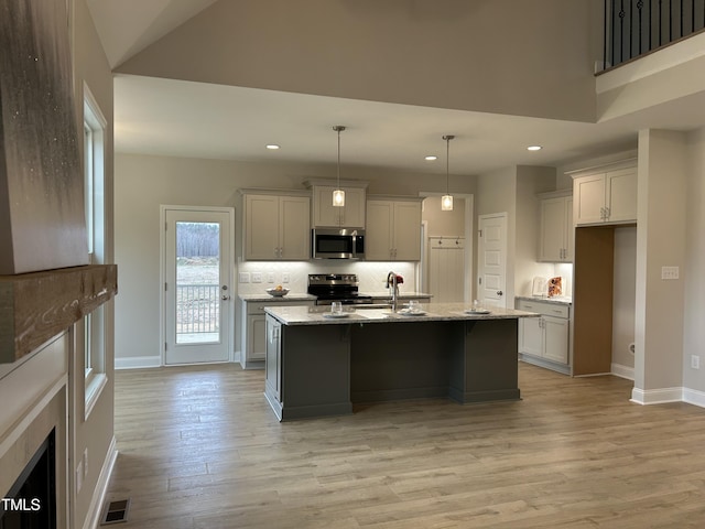 kitchen with sink, light stone counters, decorative light fixtures, stainless steel appliances, and an island with sink