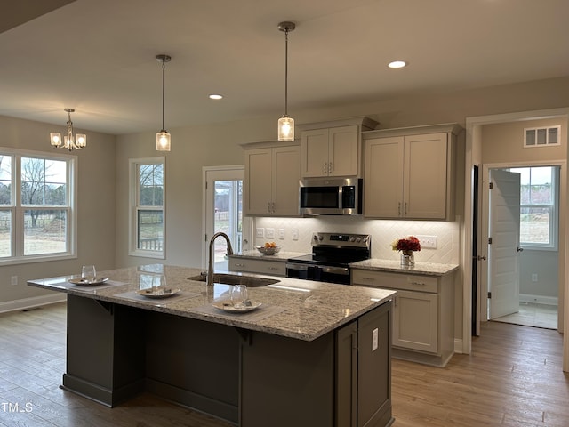 kitchen with a center island with sink, stainless steel appliances, light stone countertops, gray cabinets, and sink