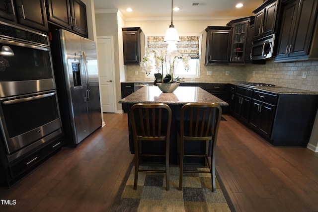 kitchen featuring appliances with stainless steel finishes, a kitchen island, backsplash, dark hardwood / wood-style flooring, and ornamental molding